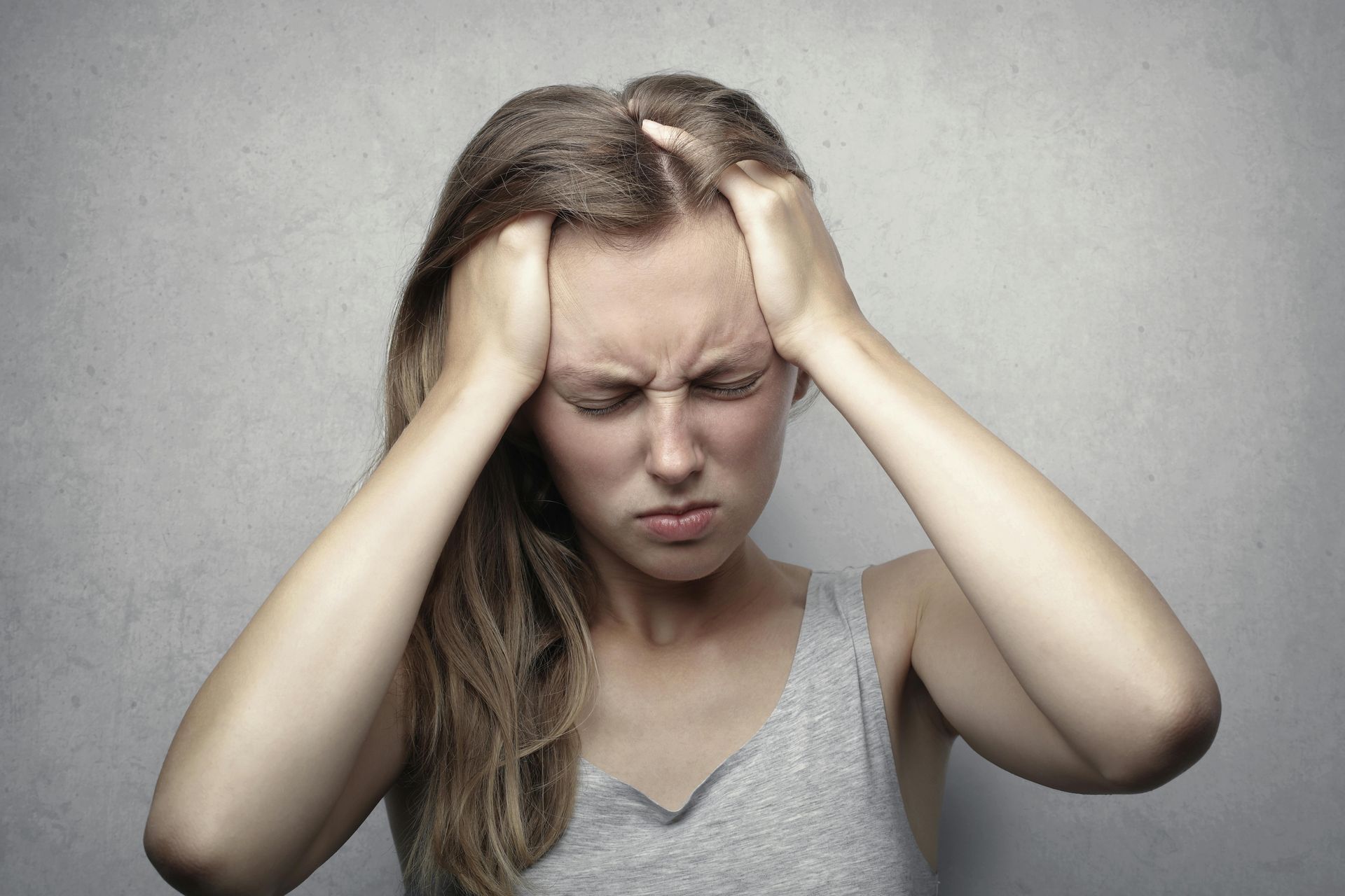 Woman holding her head with eyes closed, showing pain or stress against a gray background