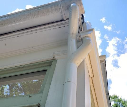 White gutters and downspout on a building exterior, against a blue sky with clouds.
