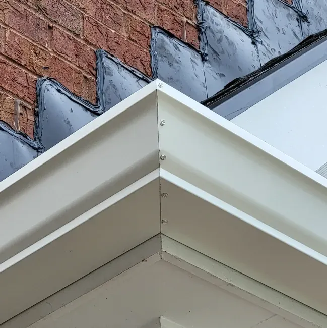 White corner guttering against a brick wall and a dark roof.