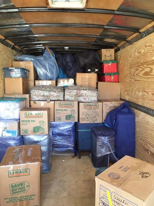 Interior of a cargo trailer packed with moving boxes and wrapped furniture.