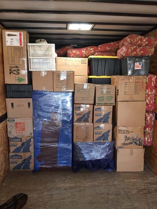A packed moving truck interior: boxes, furniture wrapped in blue plastic, and other household items.