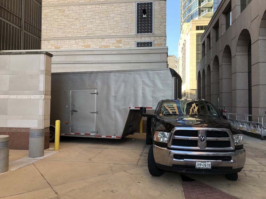 Dark pickup truck pulling a silver trailer parked between two buildings.