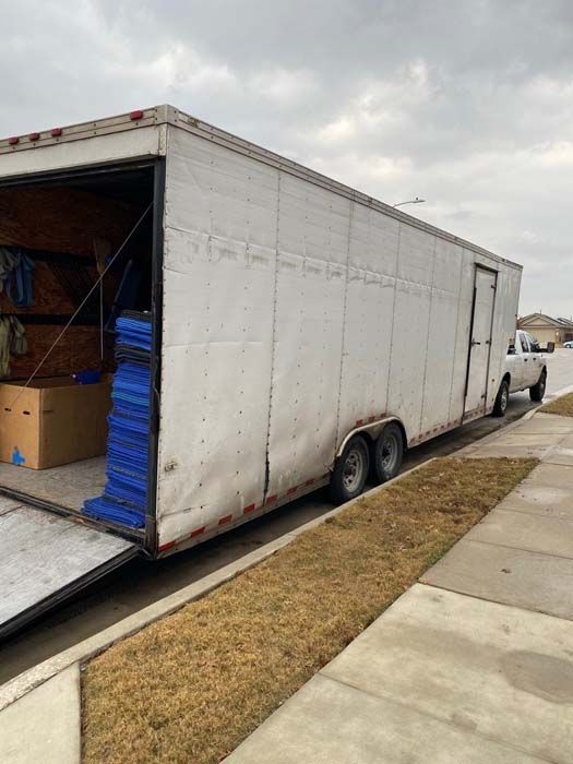 White trailer with open ramp, parked on a sidewalk. Boxes and blue pads visible inside.