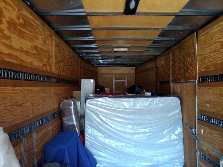 Interior of a moving truck with packed furniture: mattress, boxes, wrapped items.