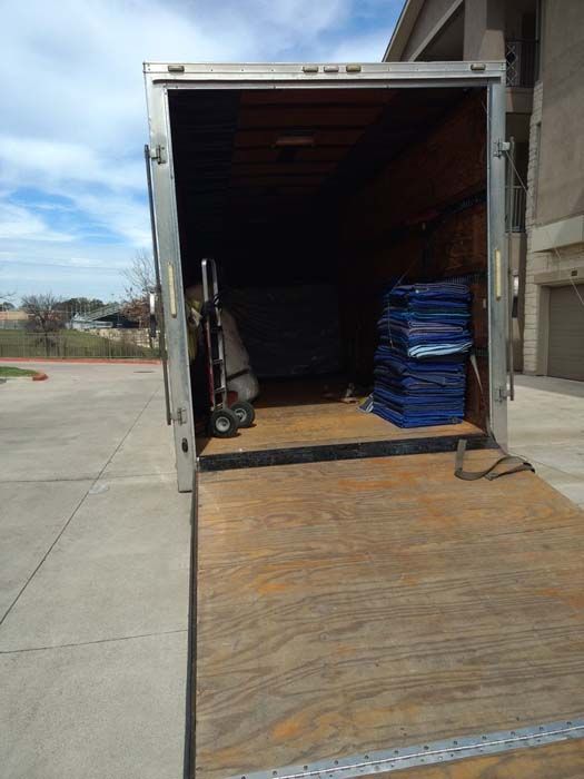 Open back of moving truck with a ramp extended, containing furniture pads and a hand truck.