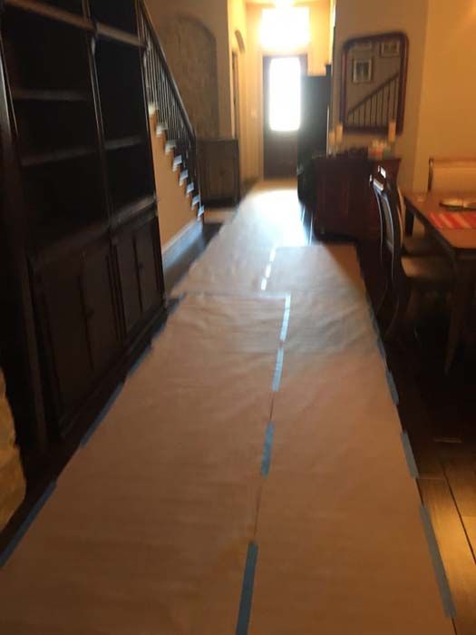 Hallway with protective paper covering the floor, dark built-in cabinet, staircase, and doorway at the end.