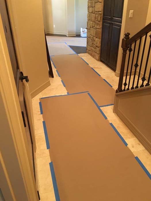 Hallway with tile floor, brown paper runners taped down with blue tape; stairs and cabinets visible.