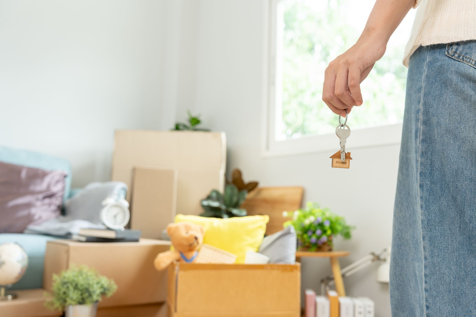 Person holding house keys in a new home, boxes and furniture in the background.