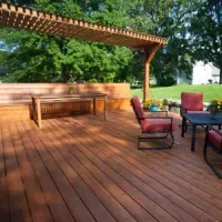 Wooden deck with pergola, bench, and patio chairs in a sunny backyard garden