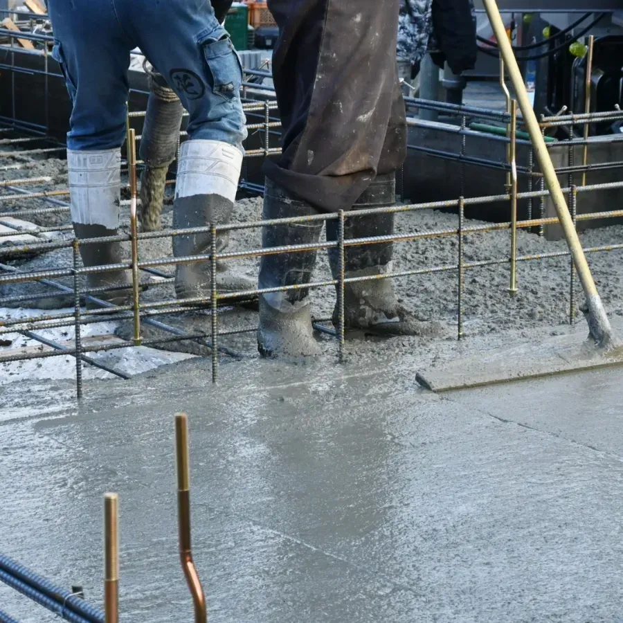 Workers pouring wet concrete into rebar foundation at a construction site