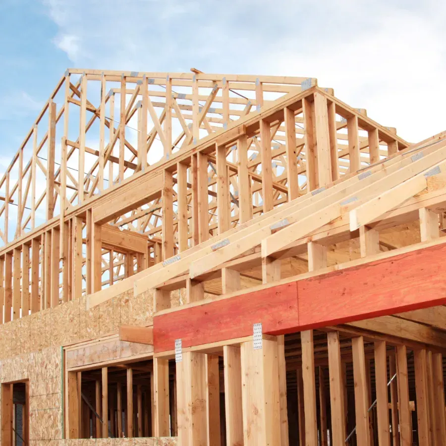 Wooden house framing under construction with exposed trusses and red beam accents