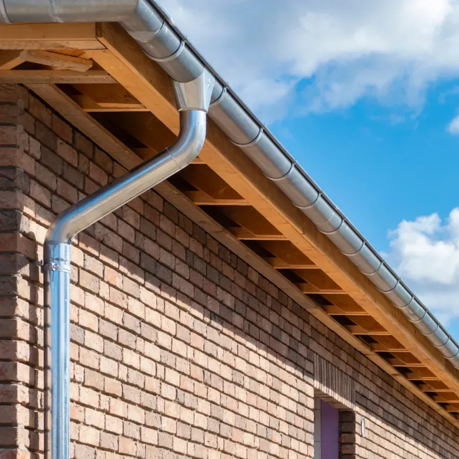 Brick house eave with white gutter against blue sky and clouds