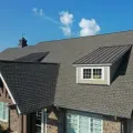 Gray shingled house roof with dormers and blue sky overhead