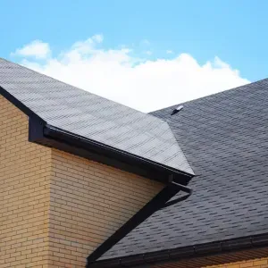 Brick house roof with dark gray shingles against a blue sky