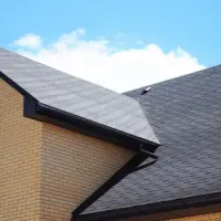 Brick house roof with dark gray shingles against a blue sky