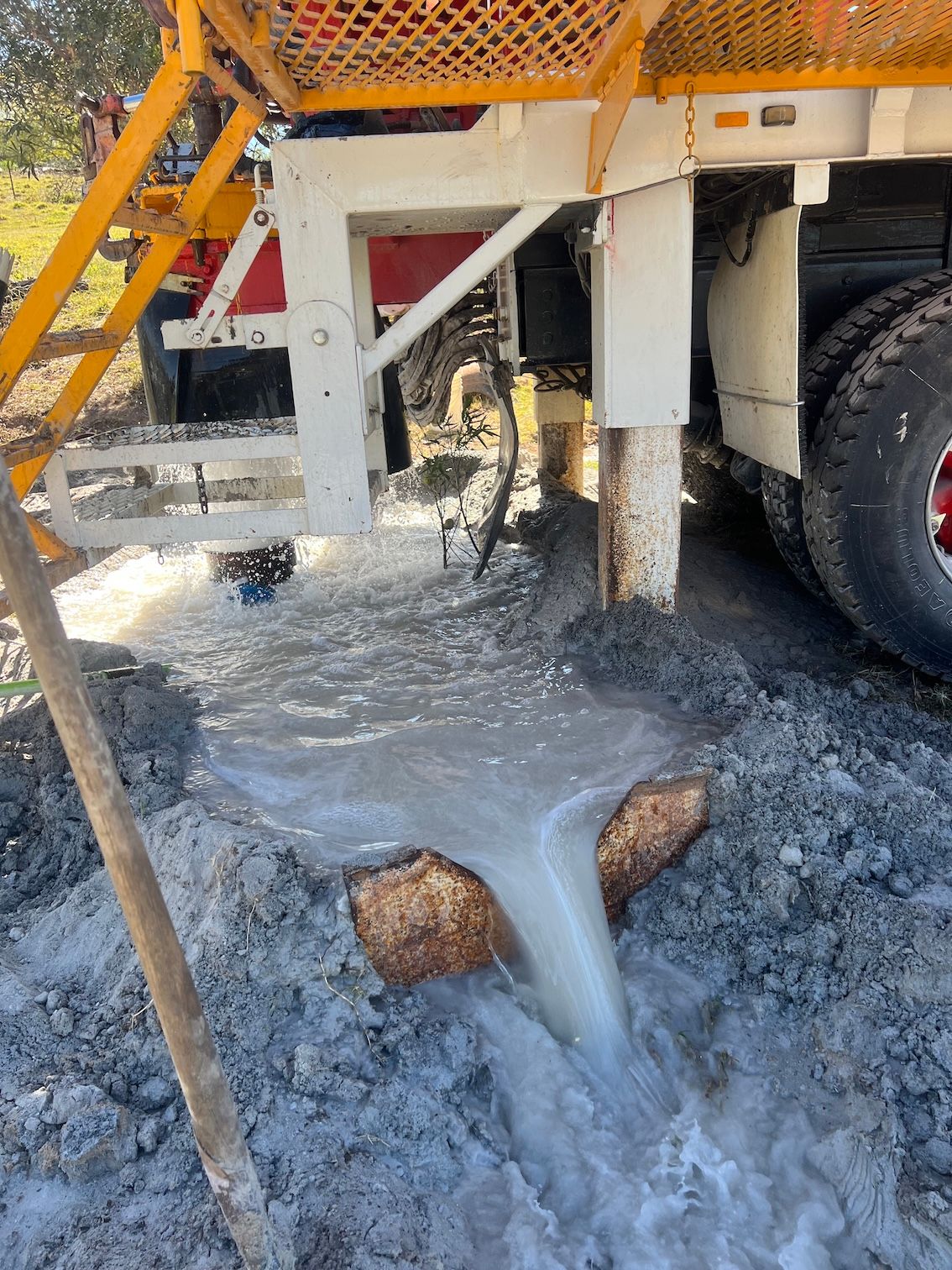 Water gushing out of a drilling site. White and red truck, yellow ladder, muddy ground — Kowaltzke Drilling Services in Gatton, QLD 