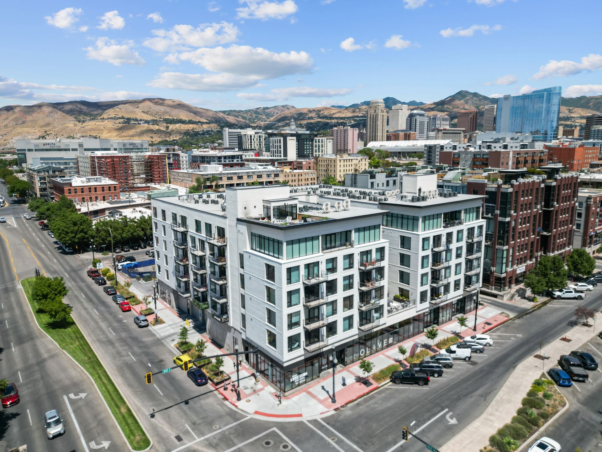 Aerial view of a white, modern apartment complex at a city street intersection with hills in the background.