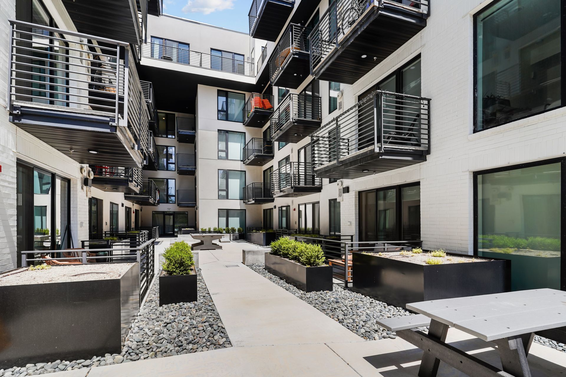 Courtyard of modern apartments with balconies, seating, and plants. White building with black accents.