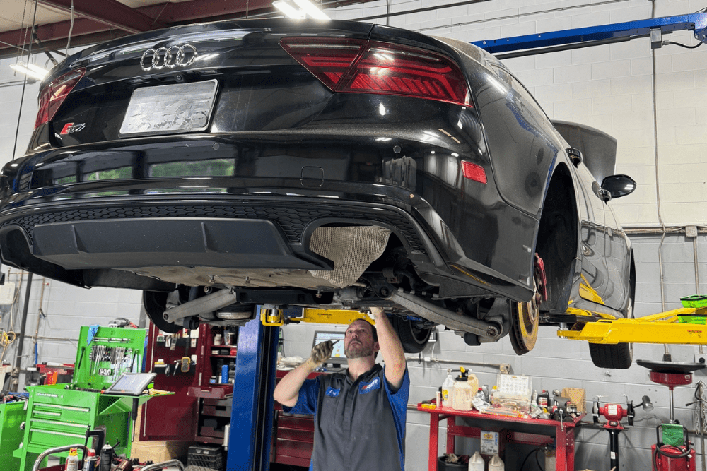 Black Audi car lifted up for technician performing repairs | AutoImports of Denver