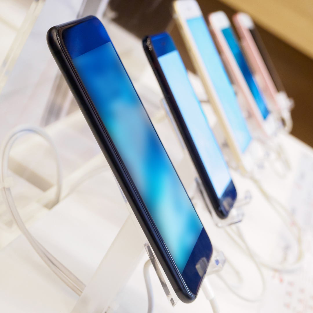Smartphones displayed on white stands in a retail store, with blue screens visible.
