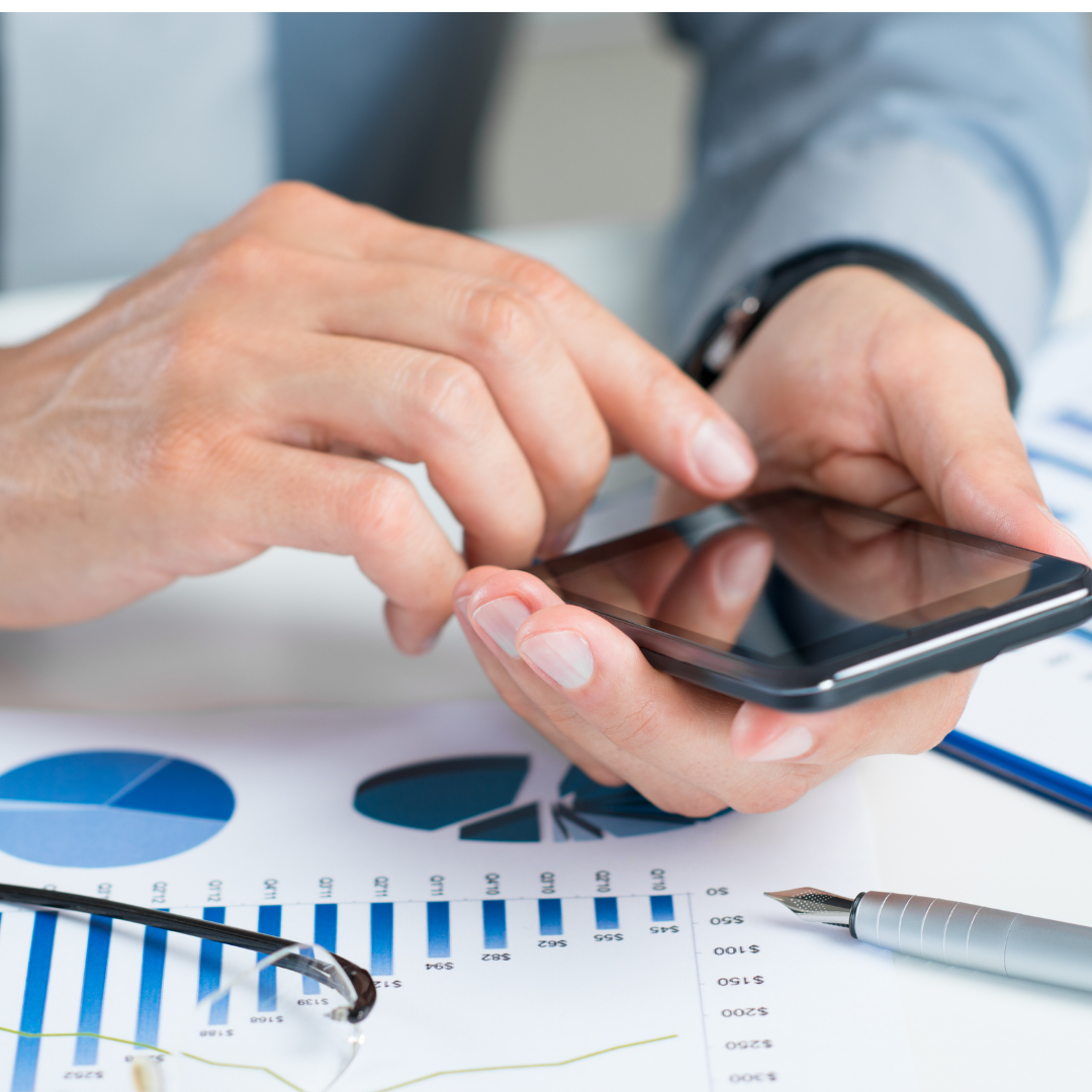 Hands using a smartphone over financial charts and a pen on a desk