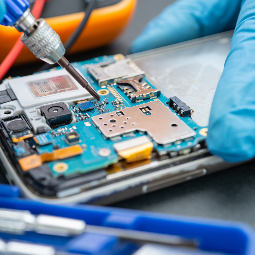 Gloved hands repairing a smartphone circuit board with a soldering tool