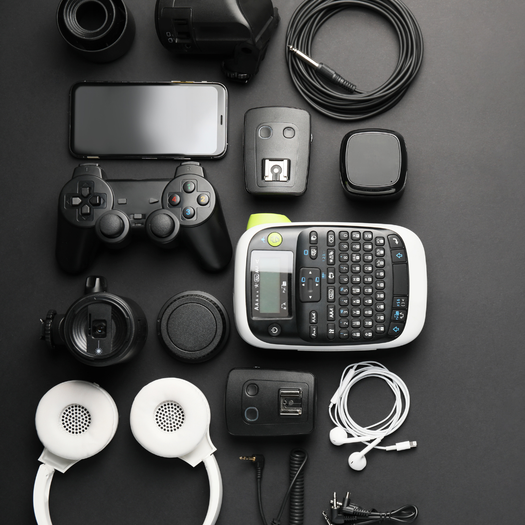 Assorted electronics and gadgets neatly arranged on a dark background, including a phone, controller, keyboard, cables