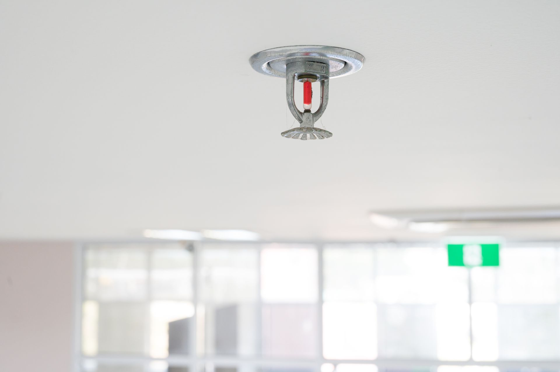 Ceiling-mounted fire sprinkler in a bright indoor space, ready for emergency activation. Ceiling-mounted fire sprinkler in a bright indoor space, ready for emergency activation.