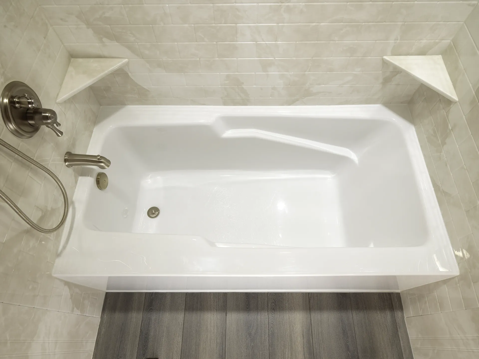 A white step-in walk-in bathtub with a side door and handheld showerhead, located next to a glass-enclosed shower.