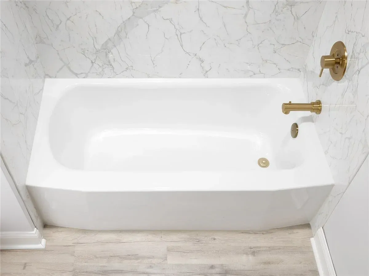 Modern bathroom with a white marble tub, glass shower enclosure, black hardware, and white storage cabinets.