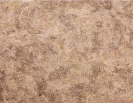 A close-up view of a textured, light brown surface with variegated marble-like patterns and subtle color swirls.