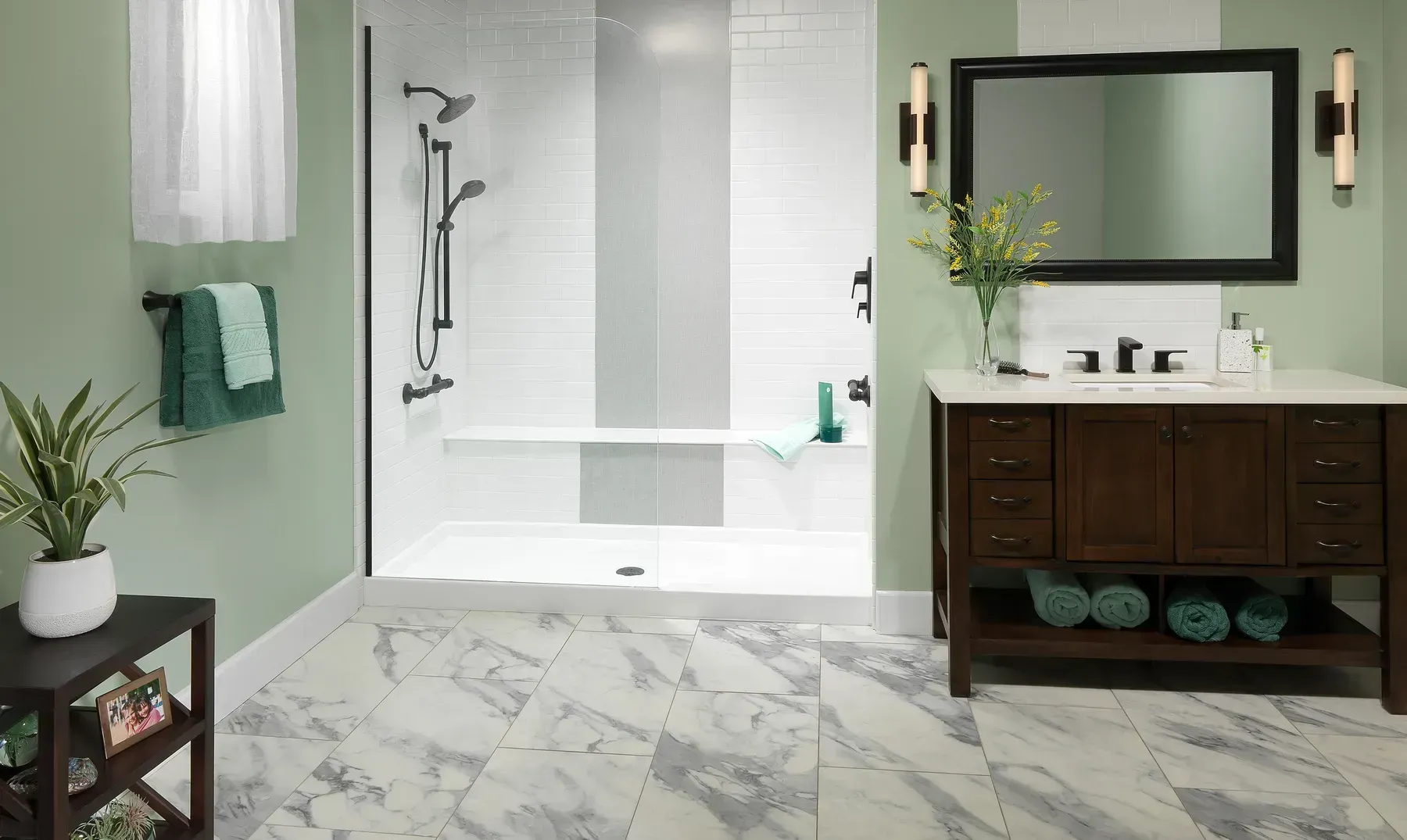 A modern bathroom with sage green walls, a walk-in shower with white tile, a dark wood vanity, and marble-look floor tiles.