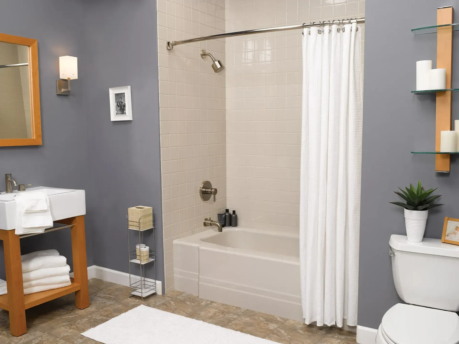 A modern bathroom with grey walls, a white tub-shower combo, a wooden vanity with white towels, and a toilet with shelving.