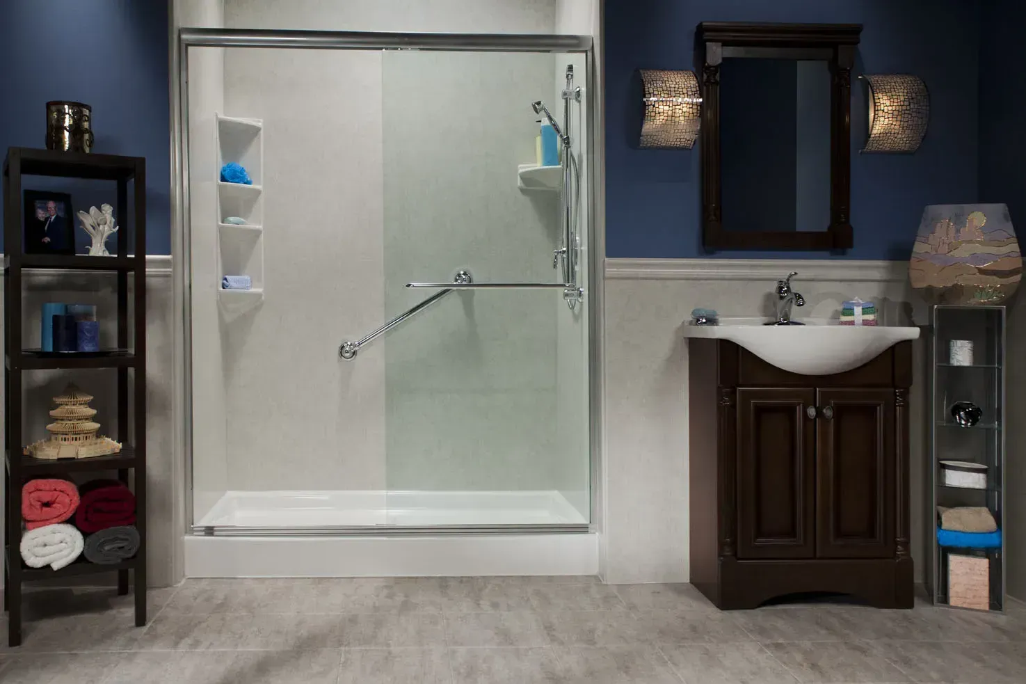 A bathroom with a white walk-in shower featuring grab bars, a brown vanity with a sink, and shelving units on both sides.