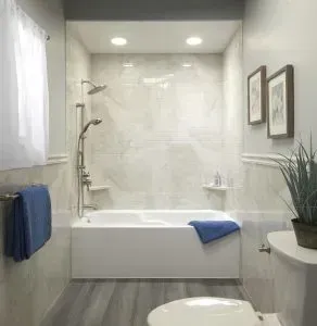 A bright, neutral-toned bathroom featuring a white bathtub, tiled shower walls, a silver showerhead, and blue towels.