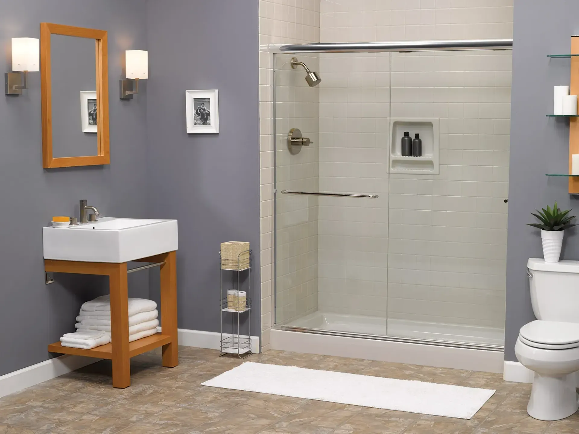 A modern bathroom featuring a white vanity with stacked towels, a glass-enclosed shower, a toilet, and gray walls.