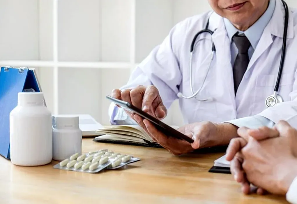 Doctor reviewing a tablet with medication and pill bottles on a desk during a consultation