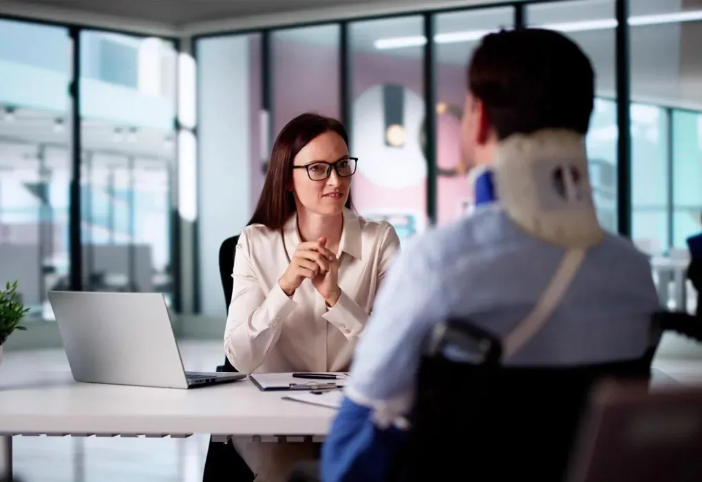Woman in glasses speaking to a seated person in a bright office meeting room