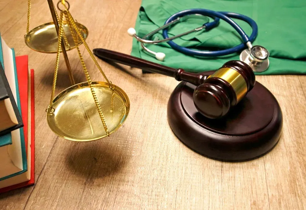 Law books, balance scale, gavel, and stethoscope on a wooden desk