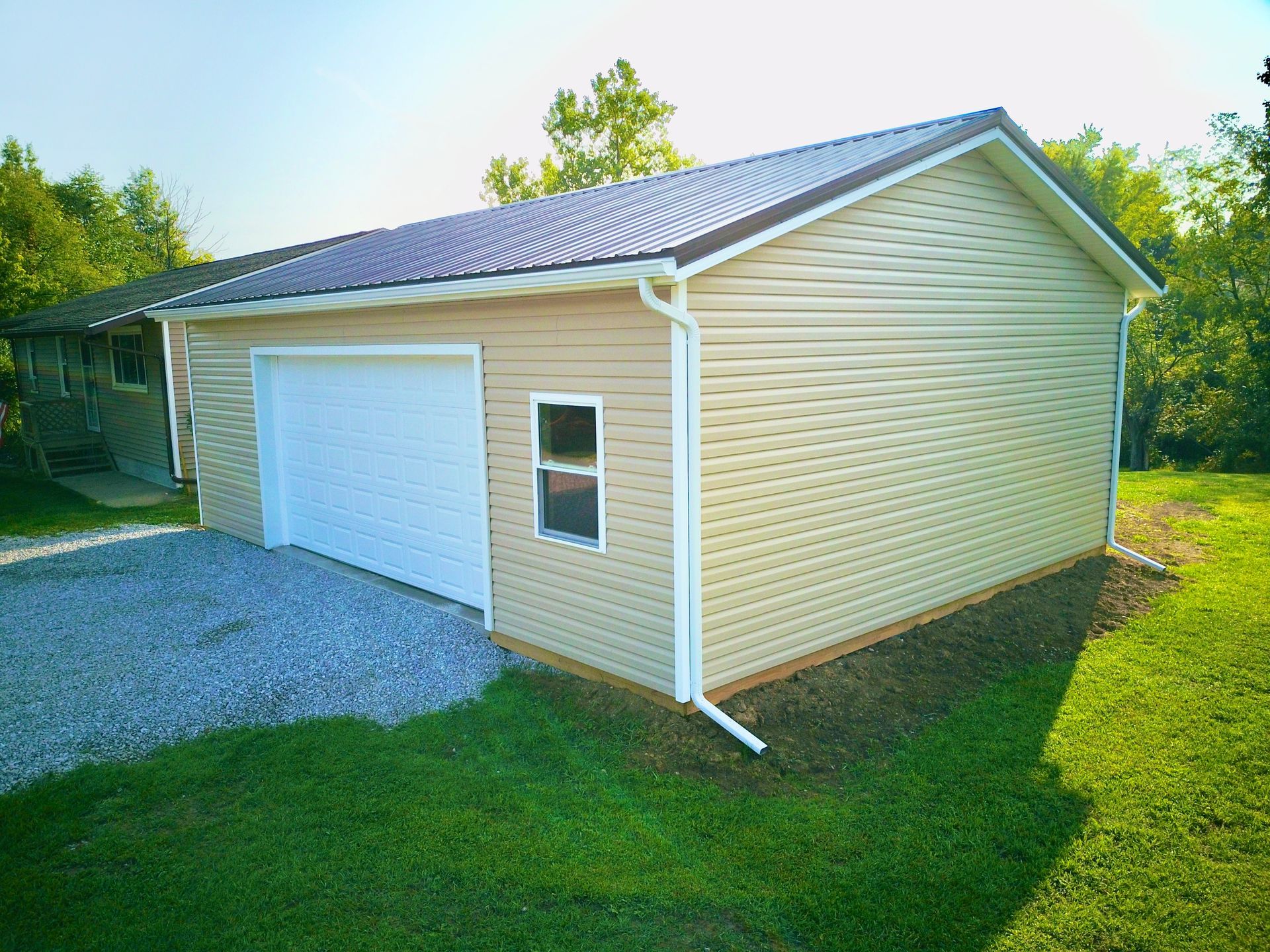 Tan garage with a white garage door, small window, and brown metal roof, set on a grassy yard.