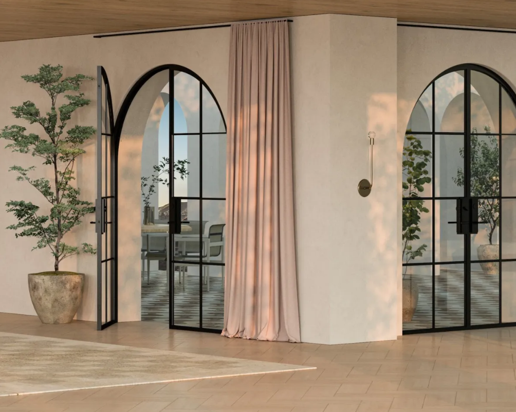 Interior with arched black steel doors and a pink curtain, sunlight, and greenery.
