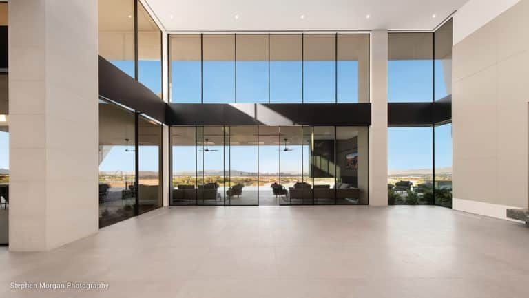 Large, open room with floor-to-ceiling windows overlooking a desert landscape; pale walls, bright blue sky.