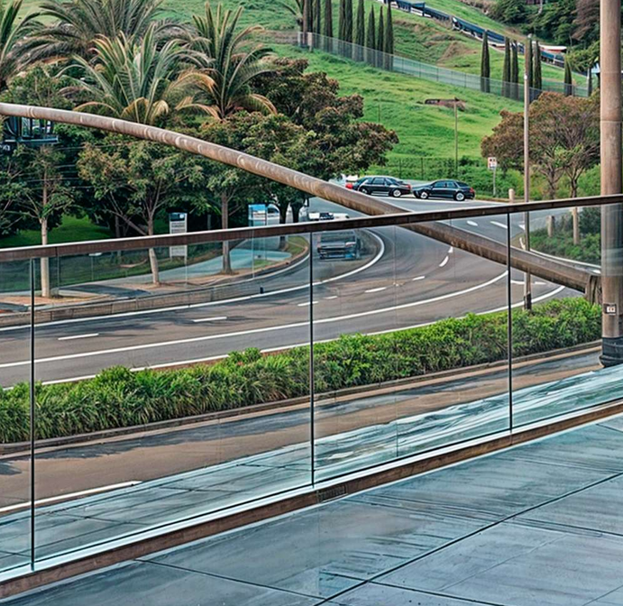Glass railing overlooking a road with cars, green hill, and palm trees.