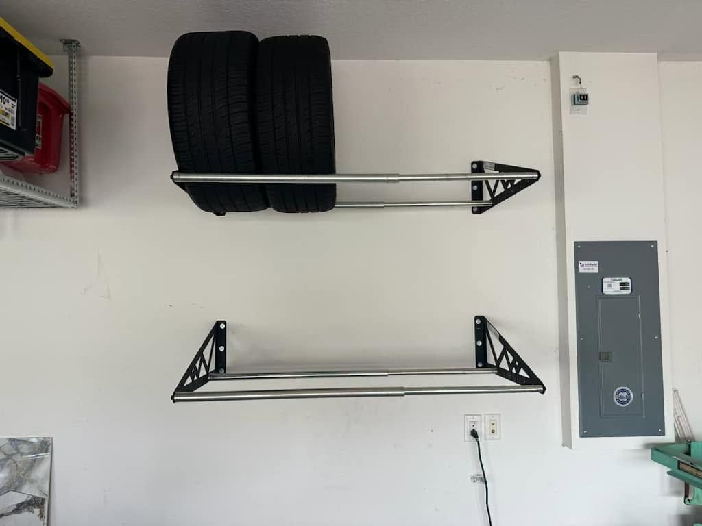 Garage wall with two mounted tire racks, one holding black tires, and a white electrical panel nearby