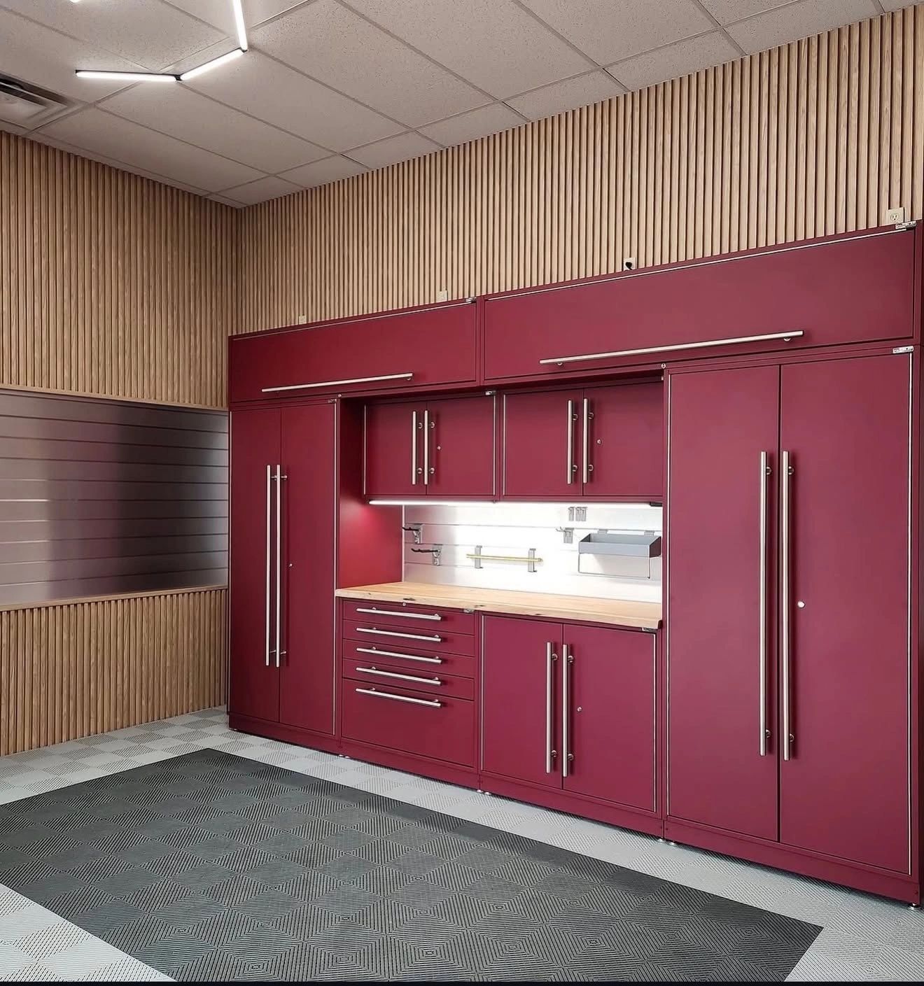 Modern garage with burgundy cabinets, wood slat walls, and gray patterned carpet.