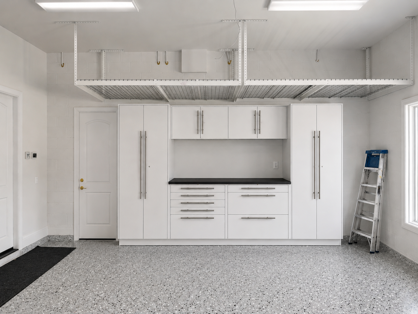 White garage interior with cabinets, workbench, overhead storage, and a folding ladder against the wall