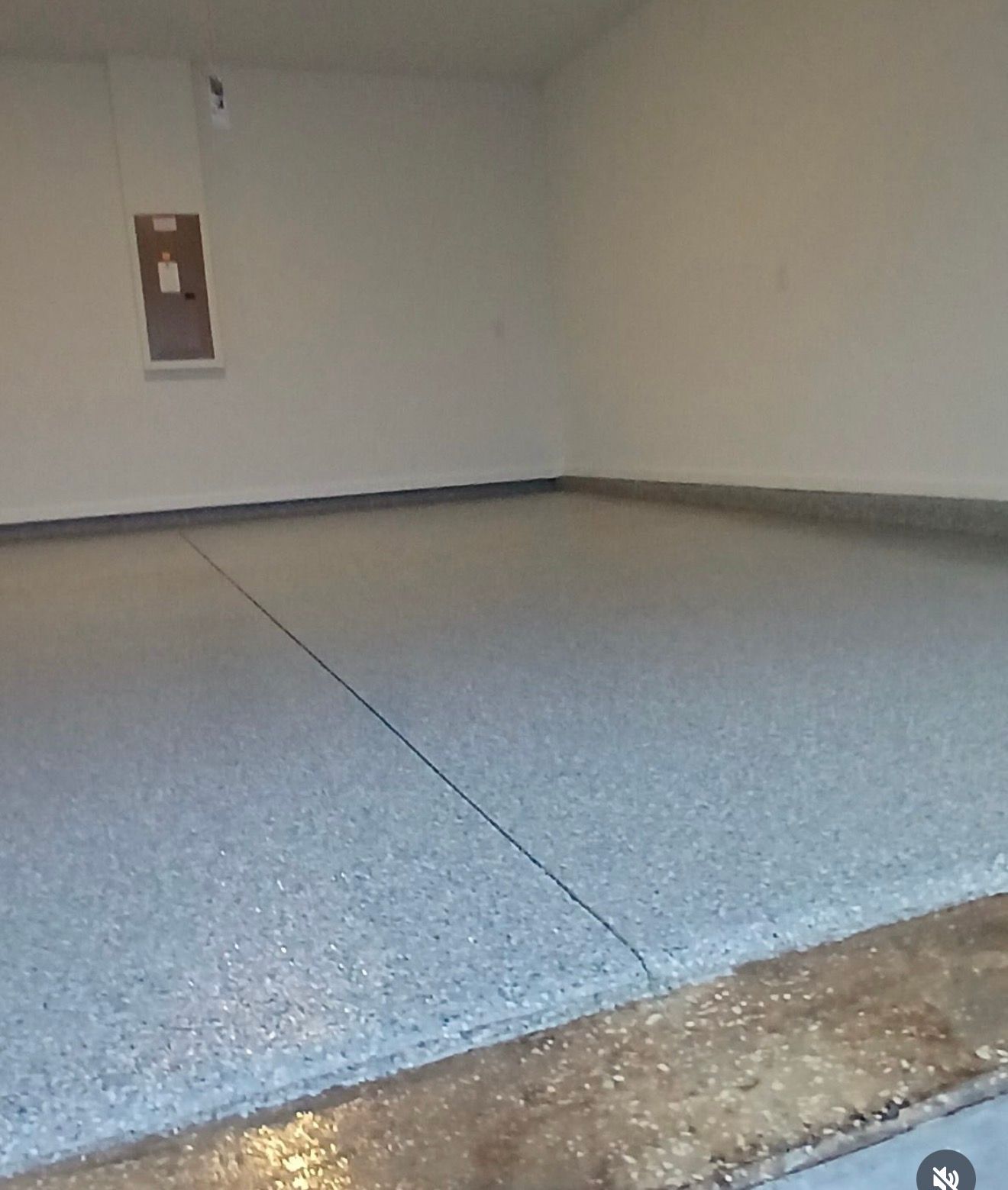 Empty gray-floored room with white walls and a small wall fixture in the corner