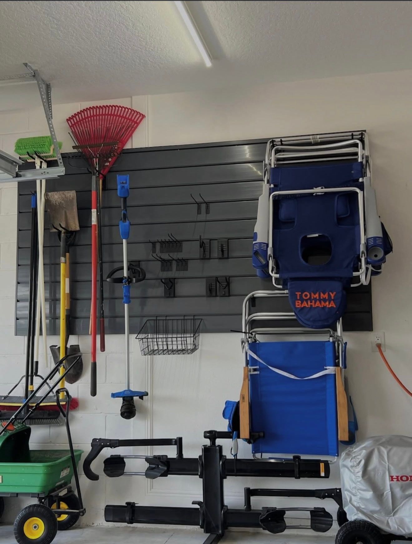 Garage wall with hanging yard tools, folded blue chair, and black scooter parts on shelves