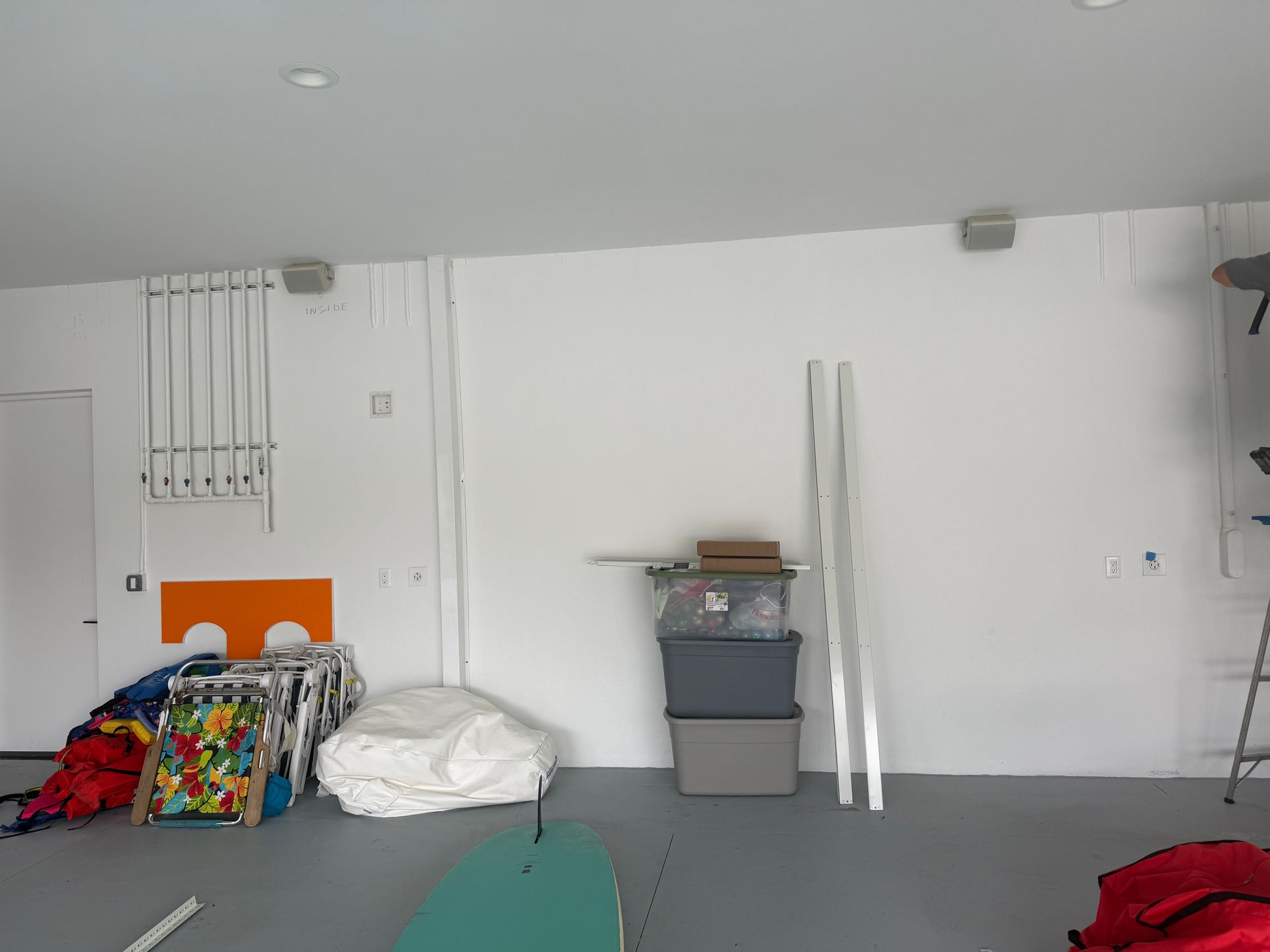 Sparse room with white walls, a gray floor, folded chairs, and stacked items in the corner.