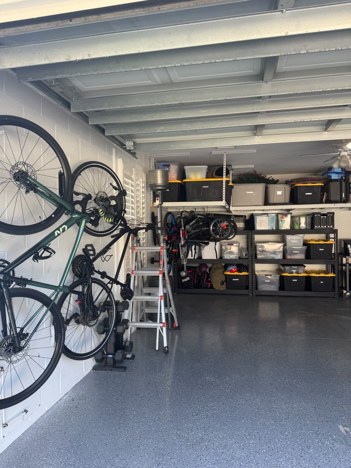 Garage with hanging bicycles, a ladder, and shelves of storage bins and tools.